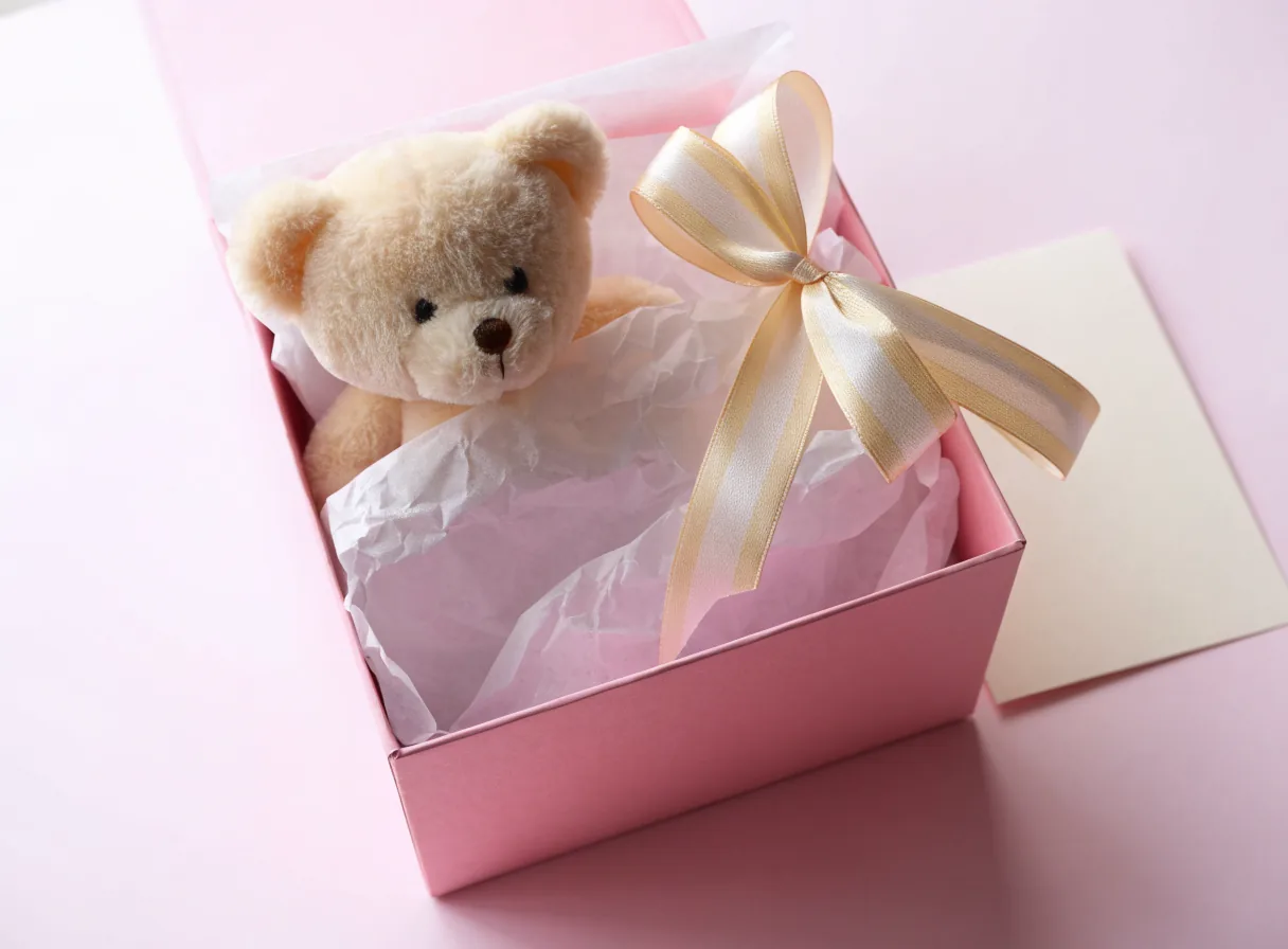 Kotak kado terbuka berisi boneka beruang krem dengan pita